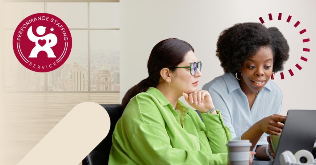 Two women sitting at a table looking at a laptop.